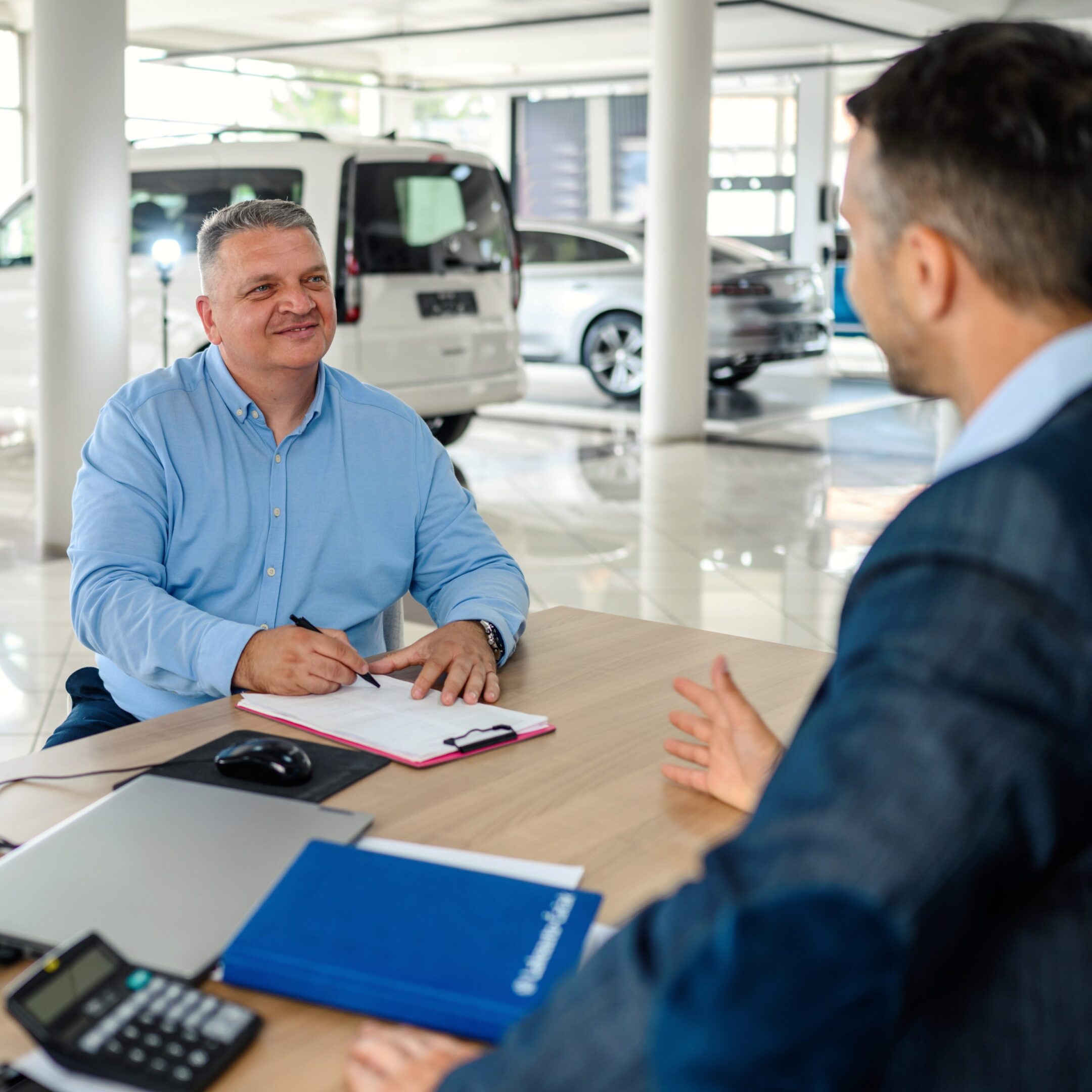 Car salesman and customer in dealership office.