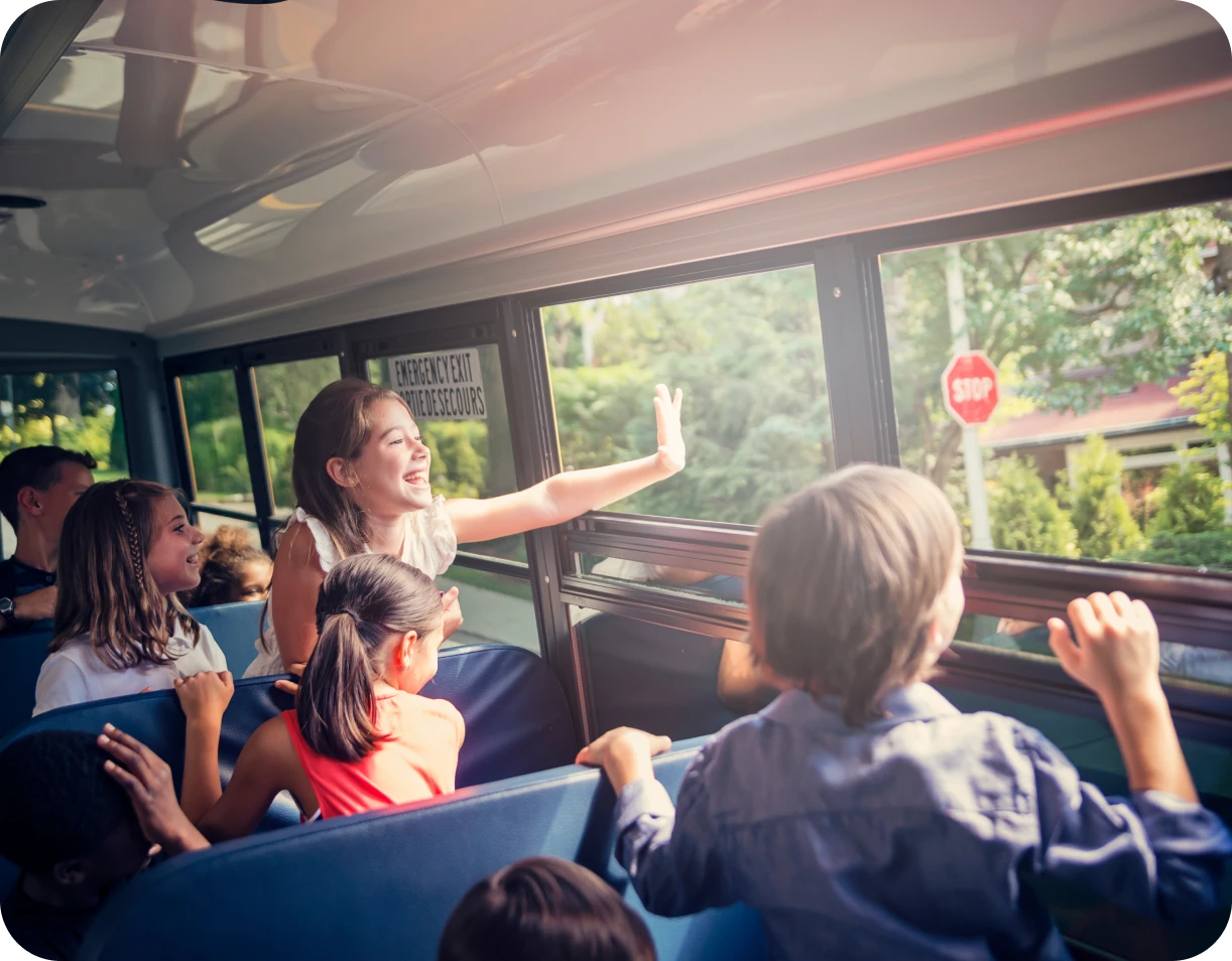 Children waving from school bus outside window.